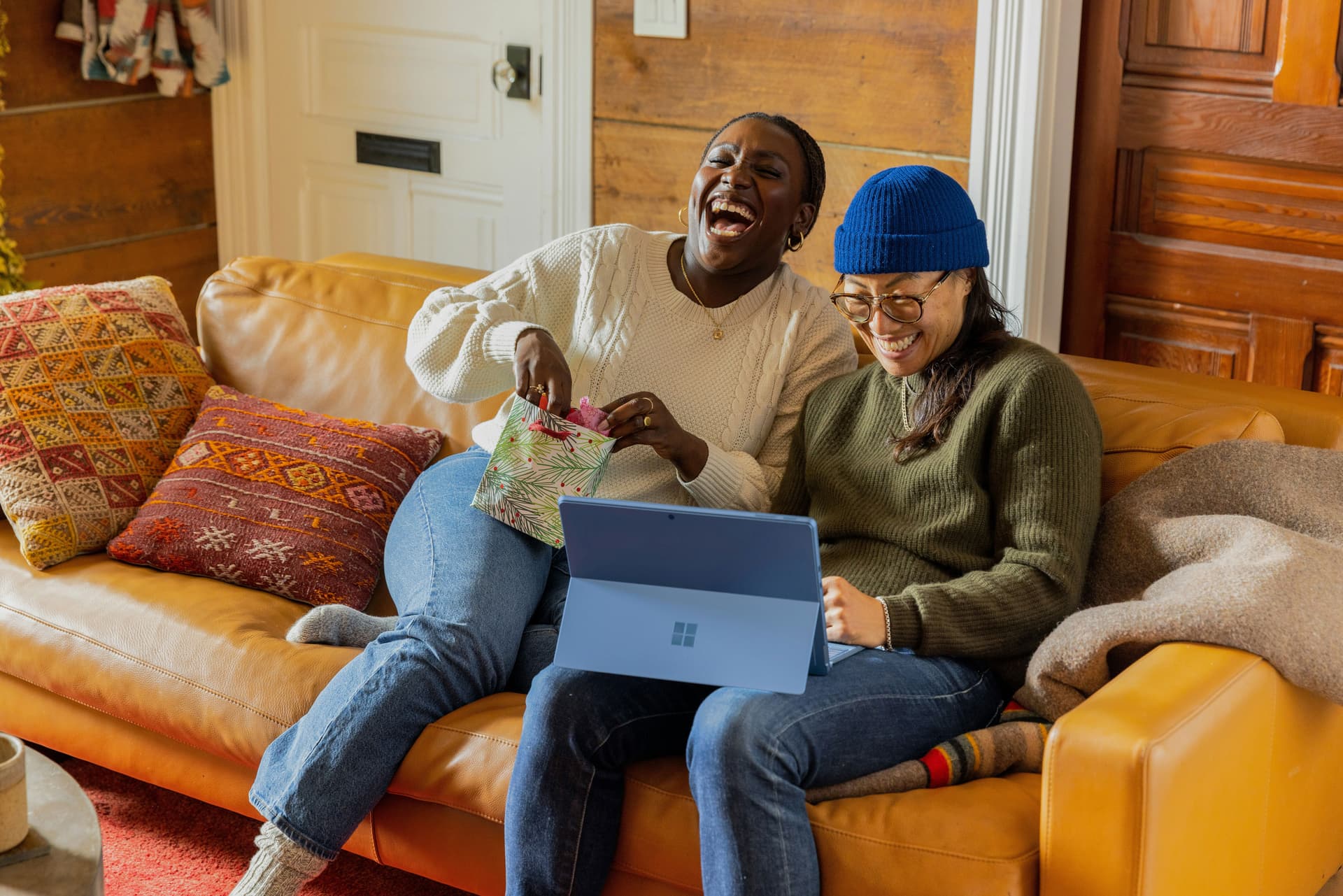 Zwei Personen lachen gemeinsam über ein Tablet auf dem Sofa