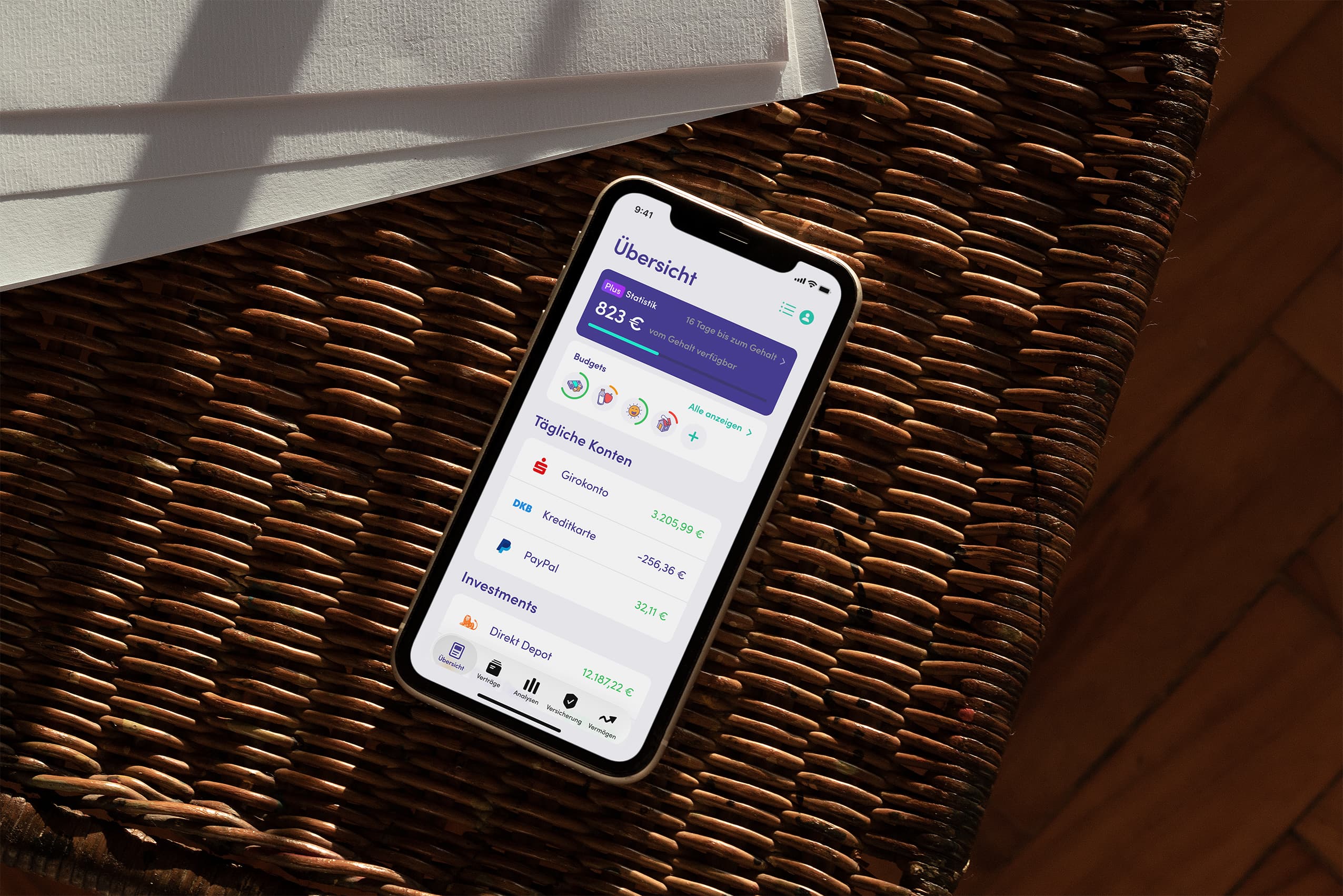 Finanzguru App auf einem iPhone, liegend auf einem Korbstuhl in warmem Sonnenlicht